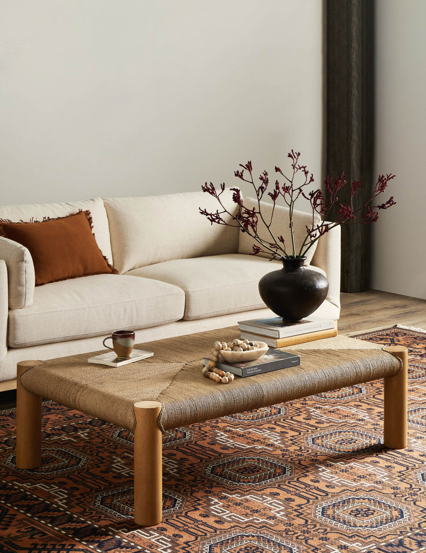 #color::natural | Lerner mahogany wood woven top coffee table styled with a cream colored sofa and orange geometric pattern area rug.