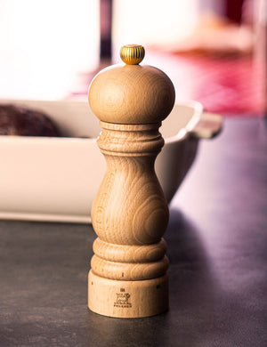 One Paris Adjustable Salt + Pepper Mill by Peugeot Saveurs sits atop a black table with a white bowl in the background