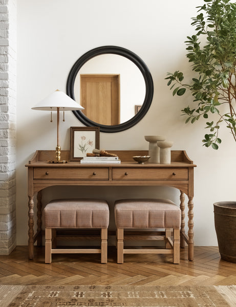 #color::black | The Bourdon Double-Framed Black Round Mirror hangs on a cream wall above a mid-century wooden desk with two ottomans