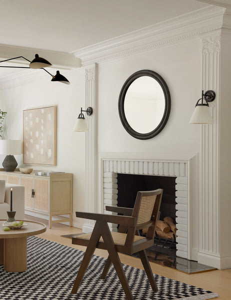 #color::black | The Bourdon Double-Framed Black Round Mirror hangs on a white wall above a fireplace and a checkerboard rug